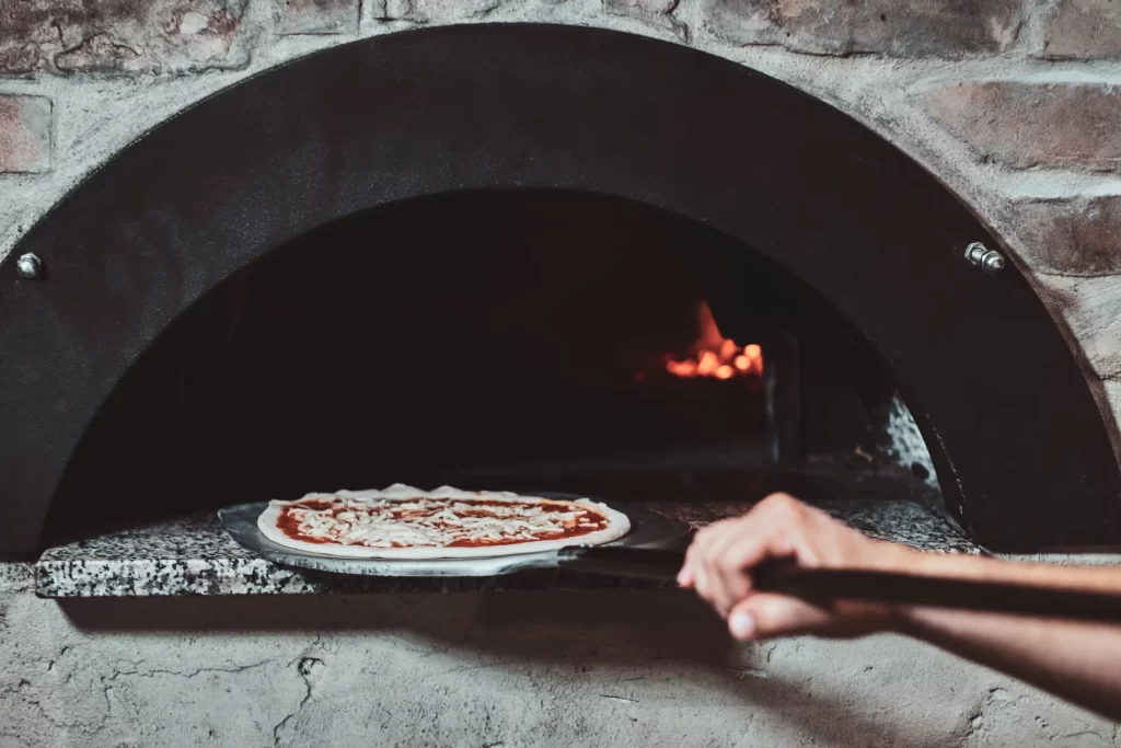 Chef sliding a margherita pizza into a wood-fired oven